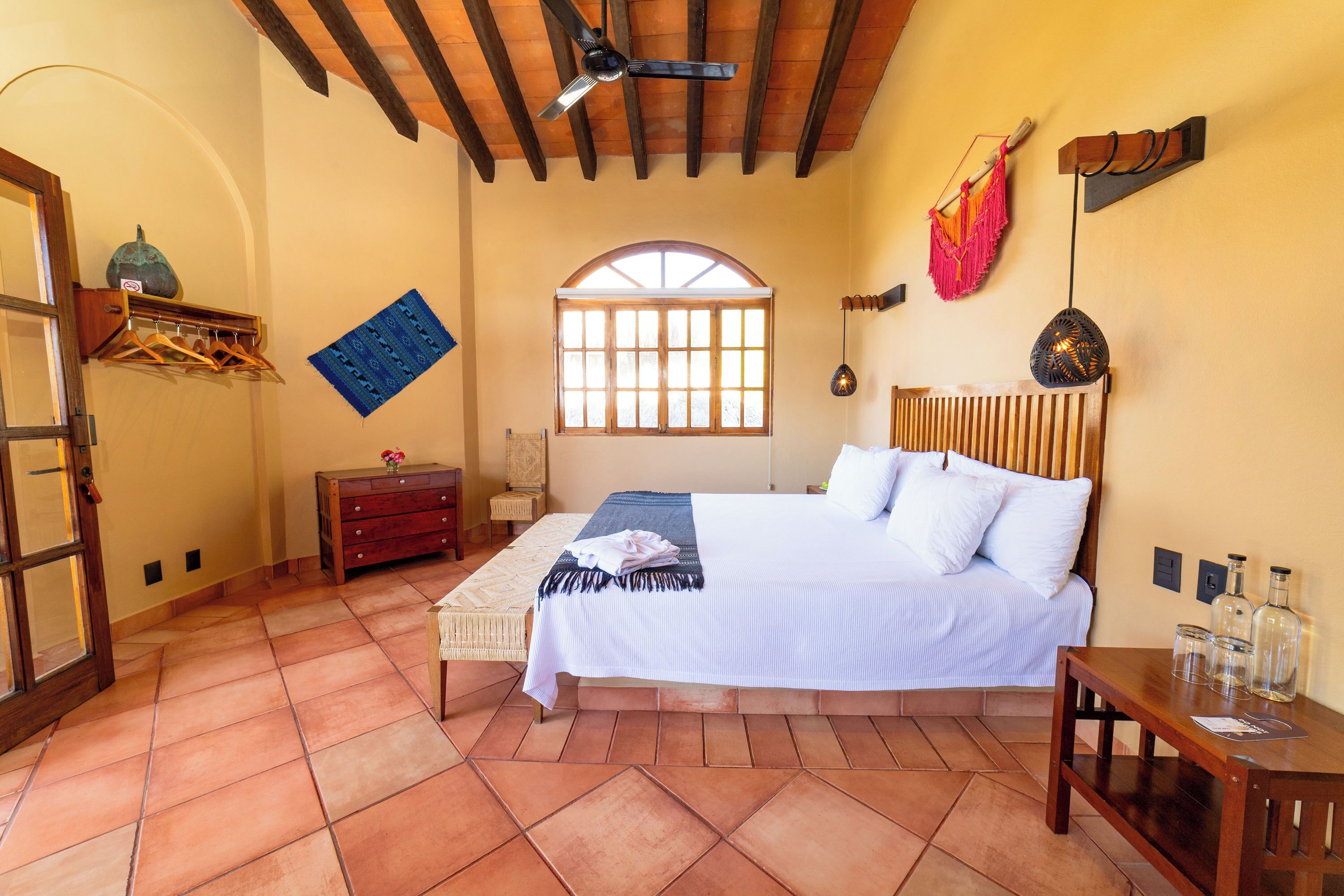 A bedroom with a large bed, a wooden ceiling, a window, and a wall-mounted shelf with bottles.