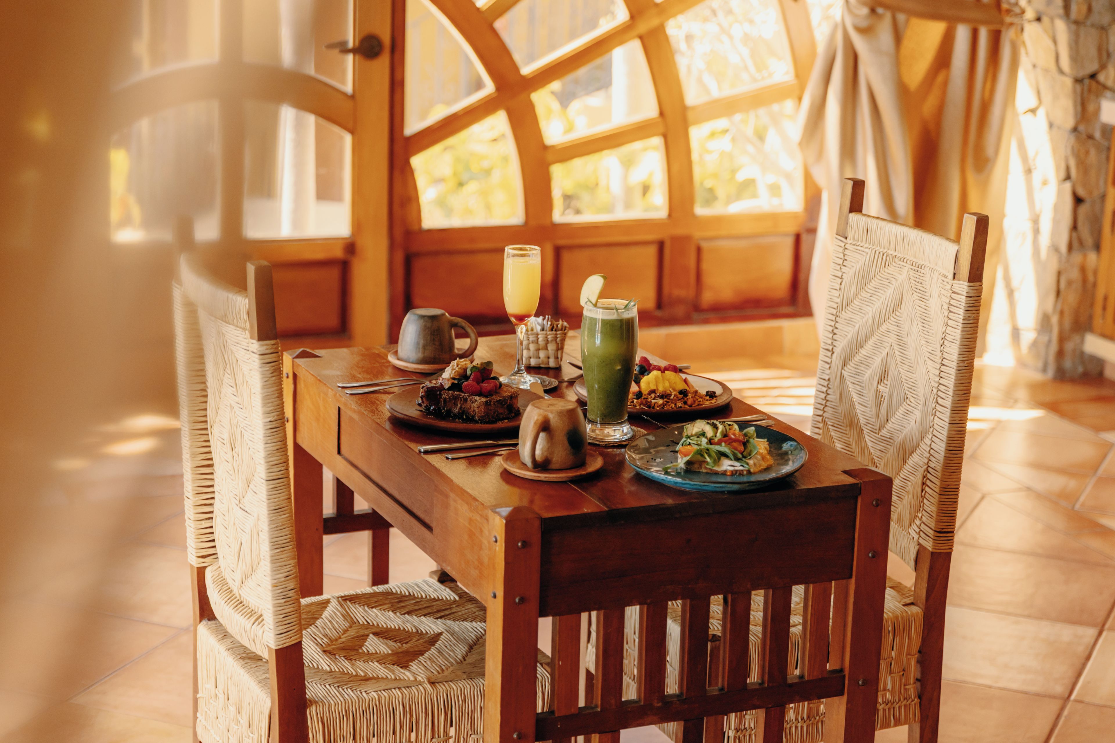 A wooden dining table with chairs, a glass of juice, and plates of food.