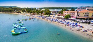 Una playa con actividades acuáticas, una hilera de sombrillas y edificios al fondo.