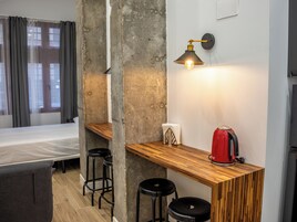 Ein kleines Hotelzimmer mit einem Bett, einer Holztrennwand, einem roten Wasserkocher und einer Wandleuchte.