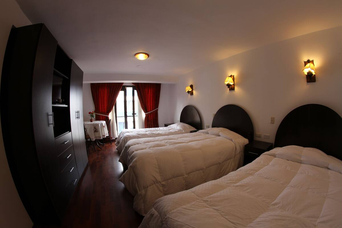 Habitación de hotel con tres camas, un escritorio y un televisor.