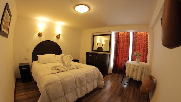 A hotel room with a large bed, a nightstand, a dresser, a mirror, a small table with a vase, and a red curtain. - La Estacion Cusco Hotel (Cusco)