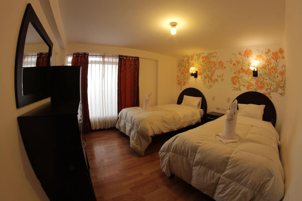 Habitación de hotel con dos camas, televisión, espejo y decoración floral en la pared.