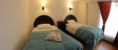 Habitación de hotel con dos camas individuales, cada una con cabecero, mesitas de noche y lámparas.