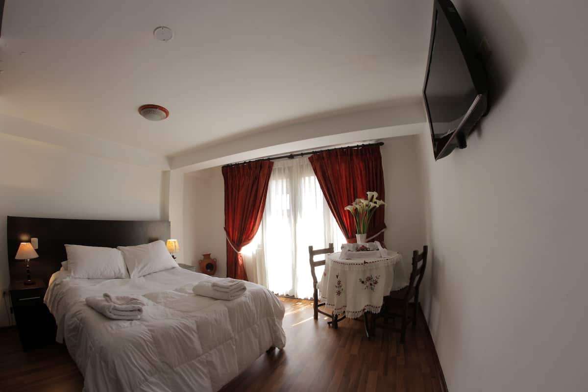Una habitación de hotel con una cama, una mesa con un florero y un televisor montado en la pared.