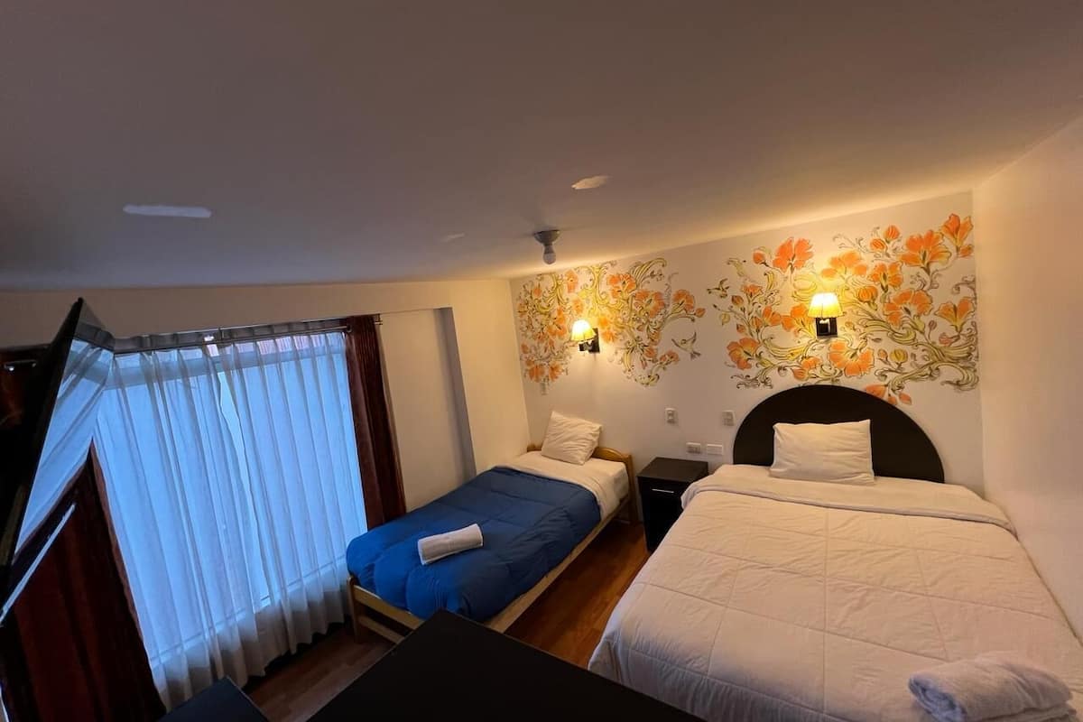 Habitación de hotel con dos camas, ventilador de techo, televisor y ventana con cortinas.