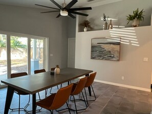 Un comedor con una mesa larga, seis sillas, un ventilador de techo y un ventanal con vistas al exterior.