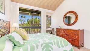 A bedroom with a bed, a wooden dresser, a round mirror, and a balcony with a view of palm trees. - "Da Koa Bar" Paradise at Turtle Bay -Trade Winds, Beaches, Sunshine Rain, Resort (Kahuku)
