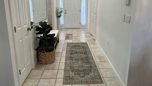 A hallway with white doors, a large mirror, a potted plant, a bench, and a rug.