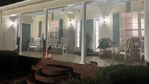 A covered porch with white columns, green shutters, and outdoor seating.