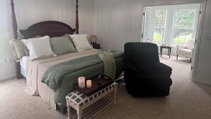 A bedroom with a four-poster bed, a bench with candles, and a black armchair.