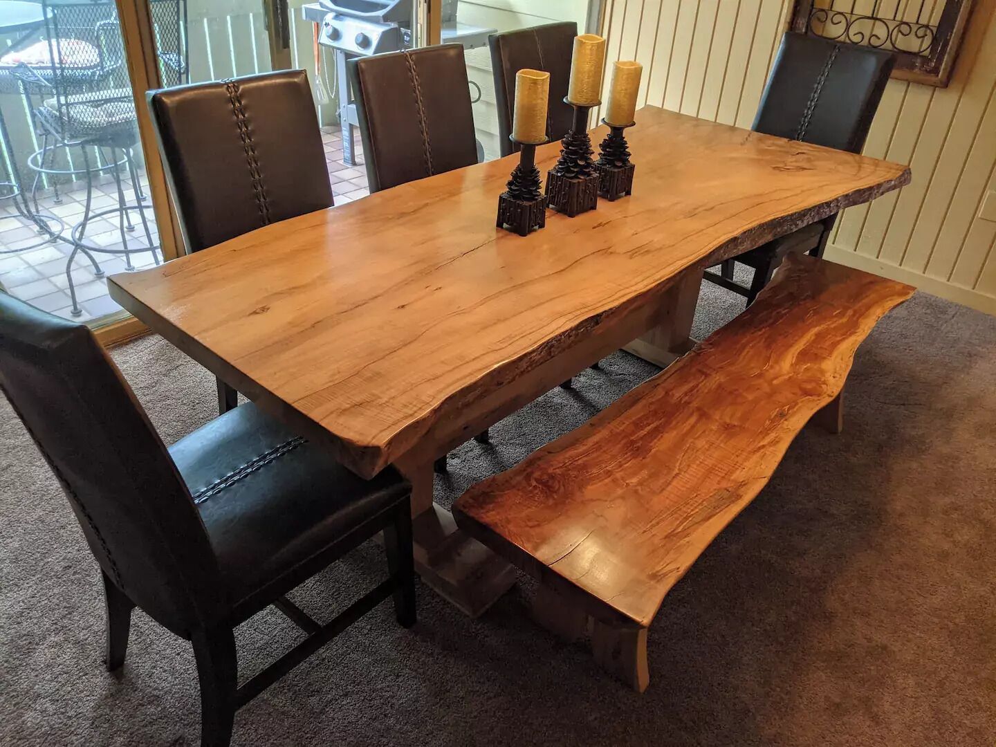 A wooden dining table with a bench, black leather chairs, and candle holders.