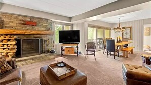 A spacious living room with a stone fireplace, a flat-screen TV, and a dining area with a chandelier. - Cozy Condo at Seven Springs
 (Champion)