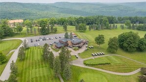 An aerial view of a golf course with a clubhouse, parking lot, and surrounding greenery. - Cozy Condo at Seven Springs
 (Champion)