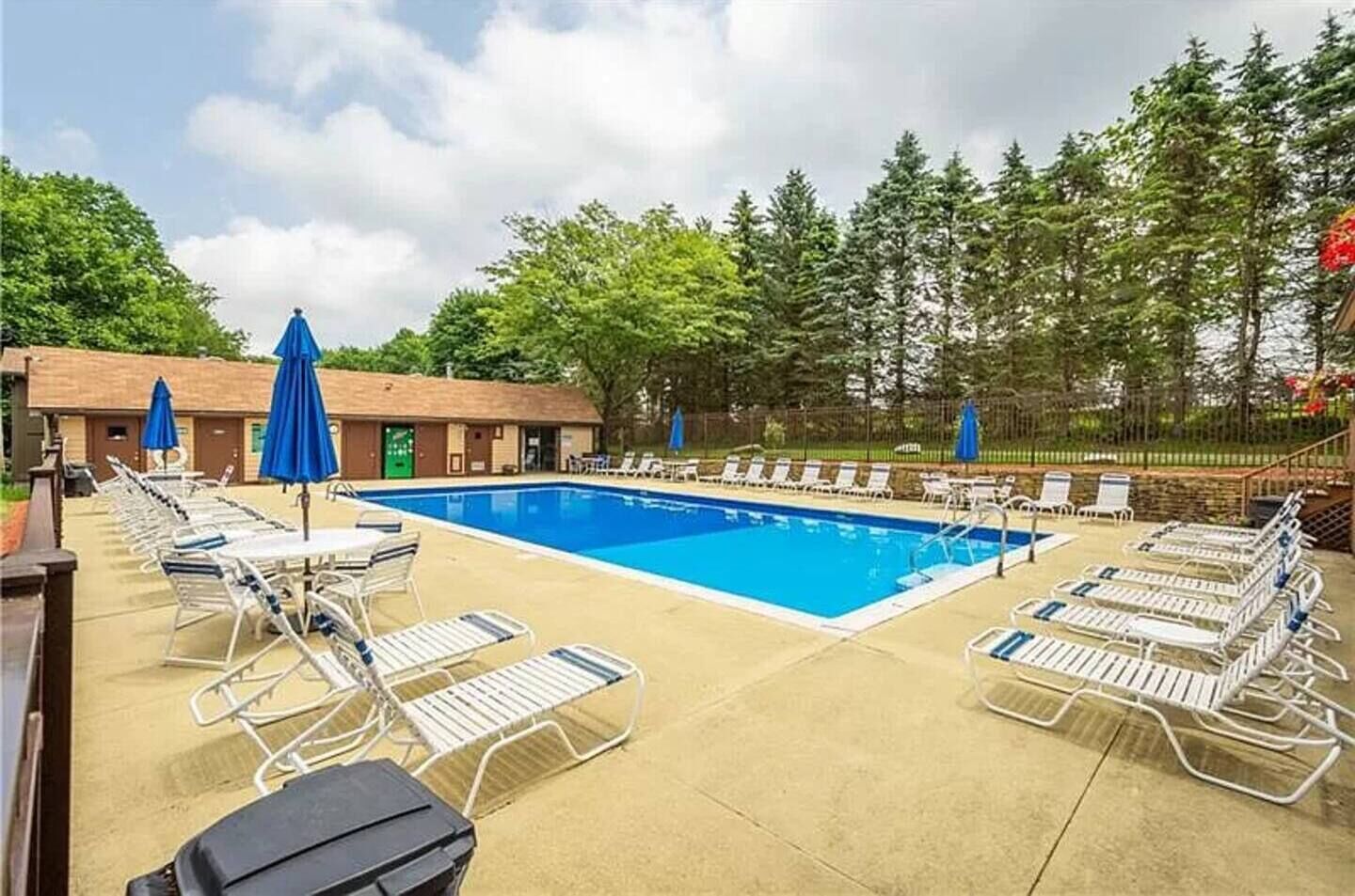 A pool area with lounge chairs and umbrellas, surrounded by trees and a building with a green door.