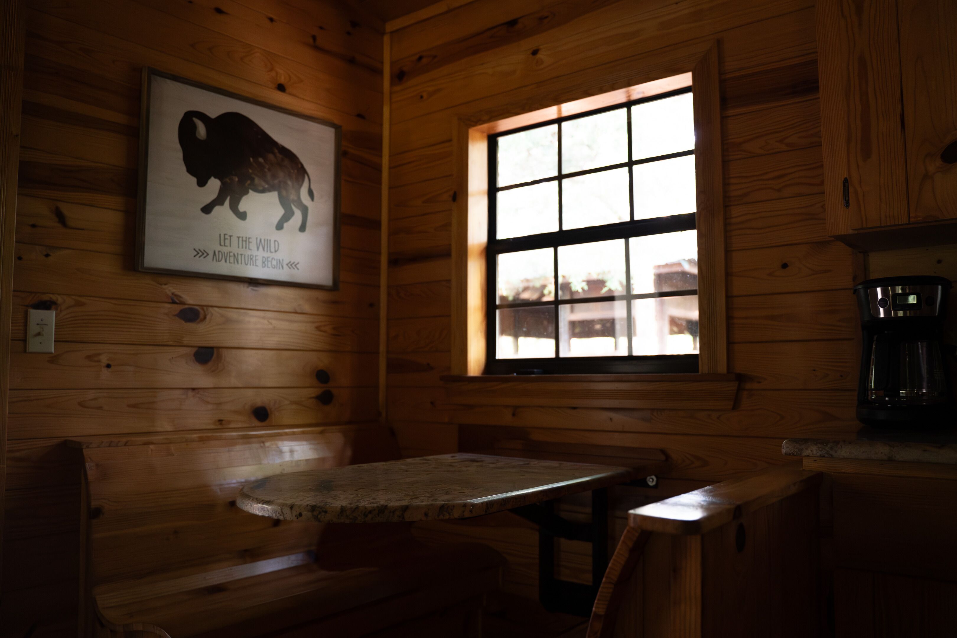 A wooden cabin interior with a wooden bench, a table, and a window with a view.