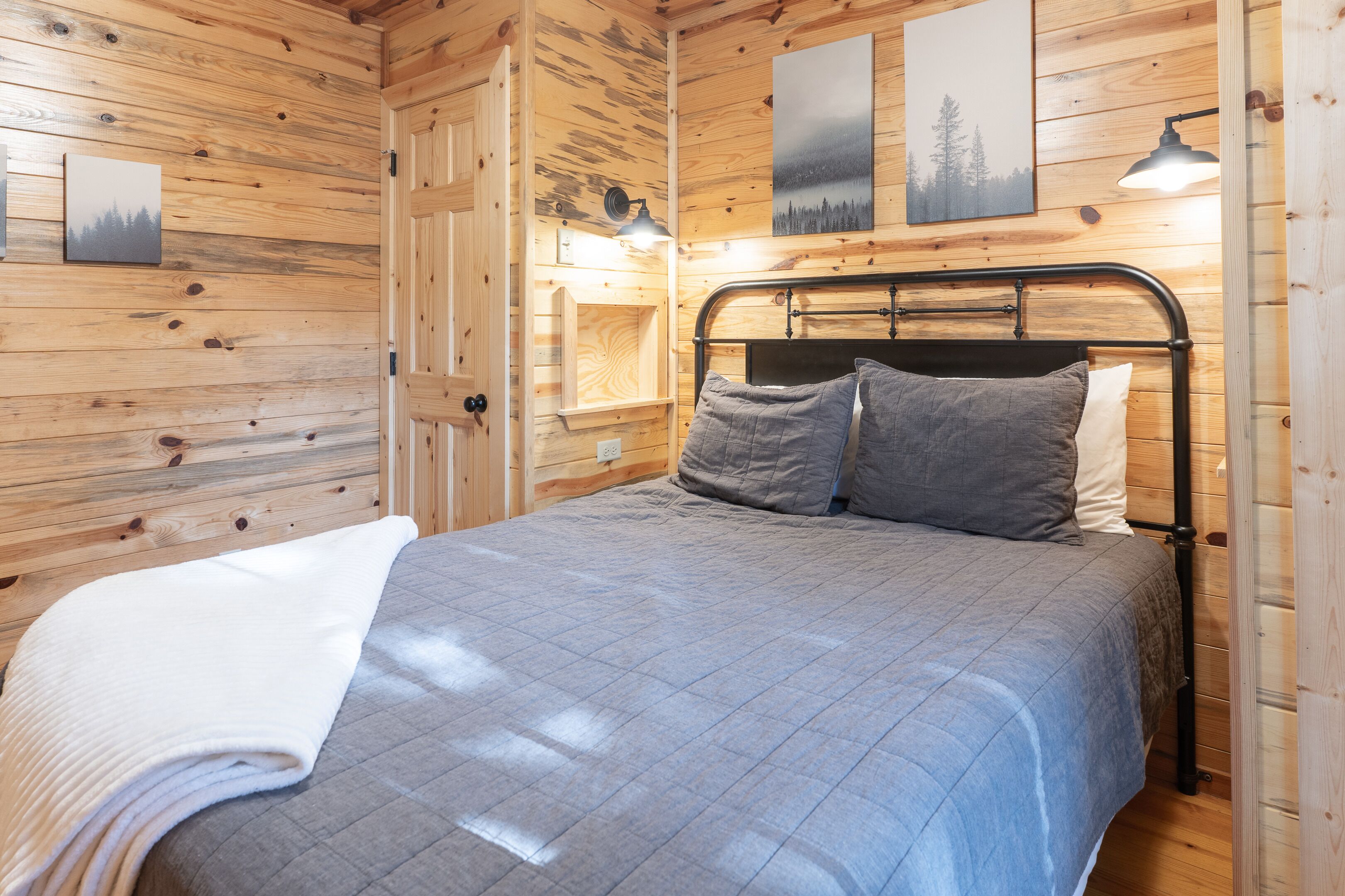 Une pièce aux murs lambrés, comprenant un lit, une table de chevet et une lampe fixée au mur.