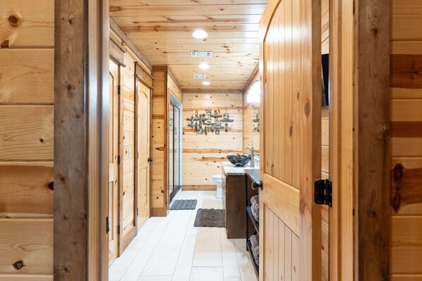 Enter a cozy cabin-style building, featuring a hallway leading to a bathroom with a sink, mirror, and towel rack.
