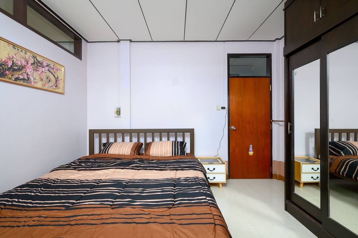 A bedroom with a bed, a nightstand, a wooden door, and a mirror.