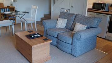 Ein Wohnzimmer mit blauem Sofa, einem Holztisch und einer Treppe, die in eine Küche mit einer Mikrowelle führt.
