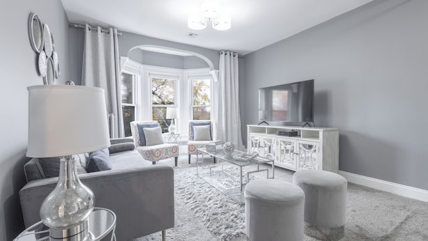 Una sala moderna con un sofá gris, una mesa de centro de vidrio y un armario blanco.