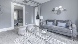 Una sala de estar moderna con un sofá gris, una mesa de centro de vidrio y una alfombra estampada.