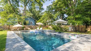 A backyard with a swimming pool, stone patio, lounge chairs, umbrellas, and a wooden fence. - Luxurious Family Escape with Small Town Charm (Montezuma)