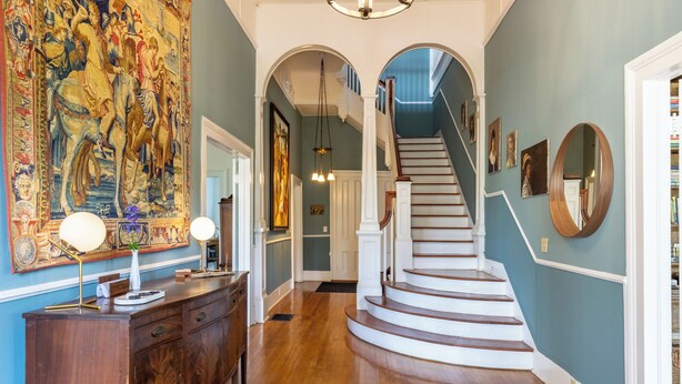 A grand hallway with a wooden staircase, a large tapestry, and a wooden desk with a lamp. - Luxurious Family Escape with Small Town Charm (Montezuma)