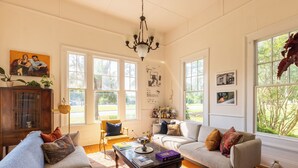 A spacious living room with two sofas, a coffee table, and a chandelier. Large windows provide natural light and views of greenery outside. - Luxurious Family Escape with Small Town Charm (Montezuma)