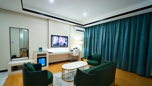 Una sala de estar moderna con un televisor de pantalla plana, un escritorio y dos sillones verdes.