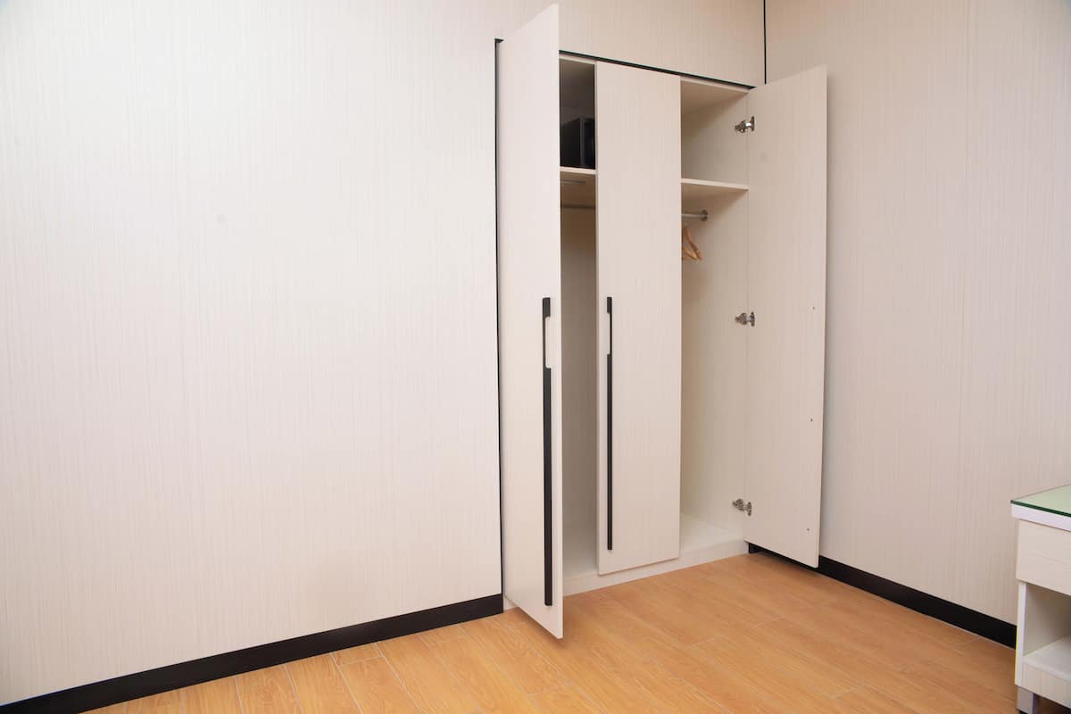 A room with a wooden floor, a white wardrobe with a mirrored door, and a white desk with a glass top.