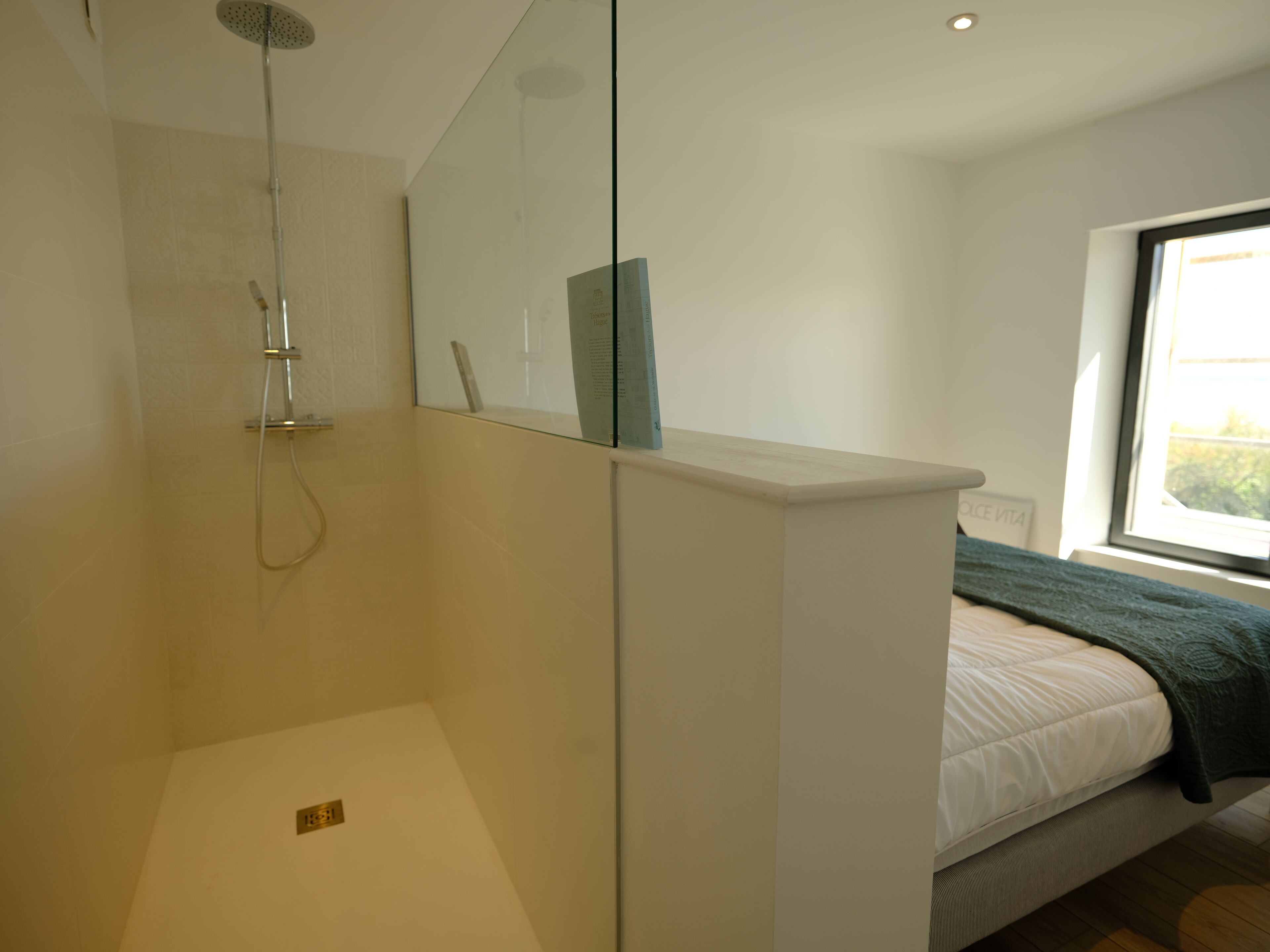 Un baño moderno con cabina de ducha de vidrio, tocador blanco y cama con manta verde.