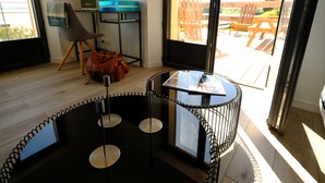 A modern room with a spiral staircase, a small table with magazines, a television, and a view of the outdoor patio. - Appartement Avec Terrasse Front de Mer, vue Imprenable sur Tatihou (Reville)
