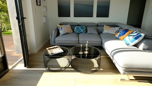 A modern living room with a grey sectional sofa, two round tables, and abstract wall art. - Appartement Avec Terrasse Front de Mer, vue Imprenable sur Tatihou (Reville)