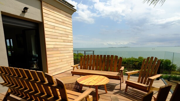 A wooden deck with outdoor furniture, including chairs and a table, overlooking a body of water. - Appartement Avec Terrasse Front de Mer, vue Imprenable sur Tatihou (Reville)