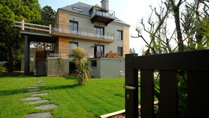 A modern two-story house with a balcony, a stone pathway, and a well-maintained lawn. - Appartement Avec Terrasse Front de Mer, vue Imprenable sur Tatihou (Reville)