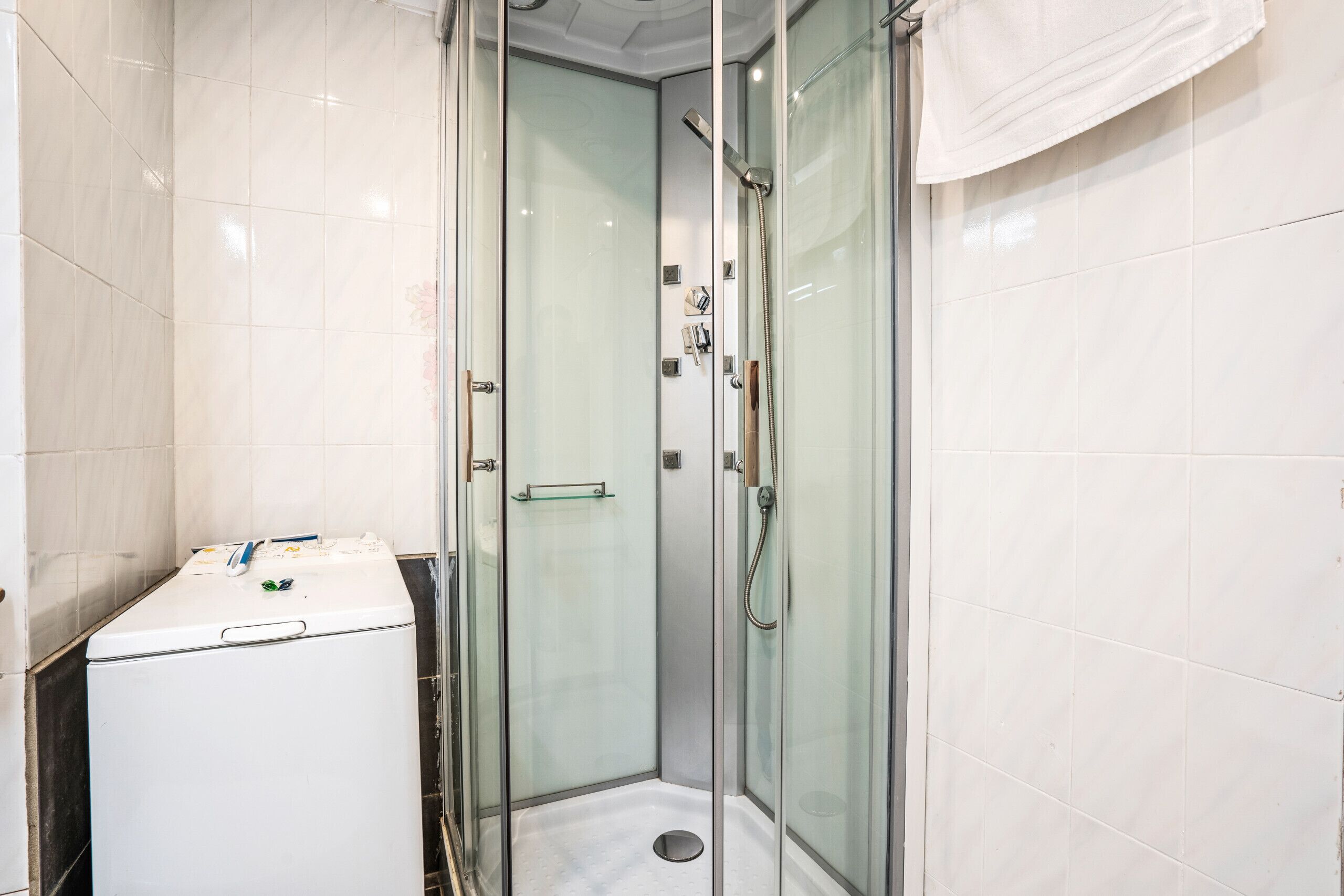 Une salle de bain moderne avec une douche à parois de verre, un lave-linge blanc et une petite étagère.