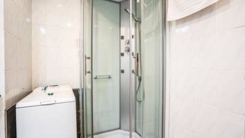 Une salle de bain moderne avec une douche à parois de verre, un lave-linge blanc et une petite étagère.
