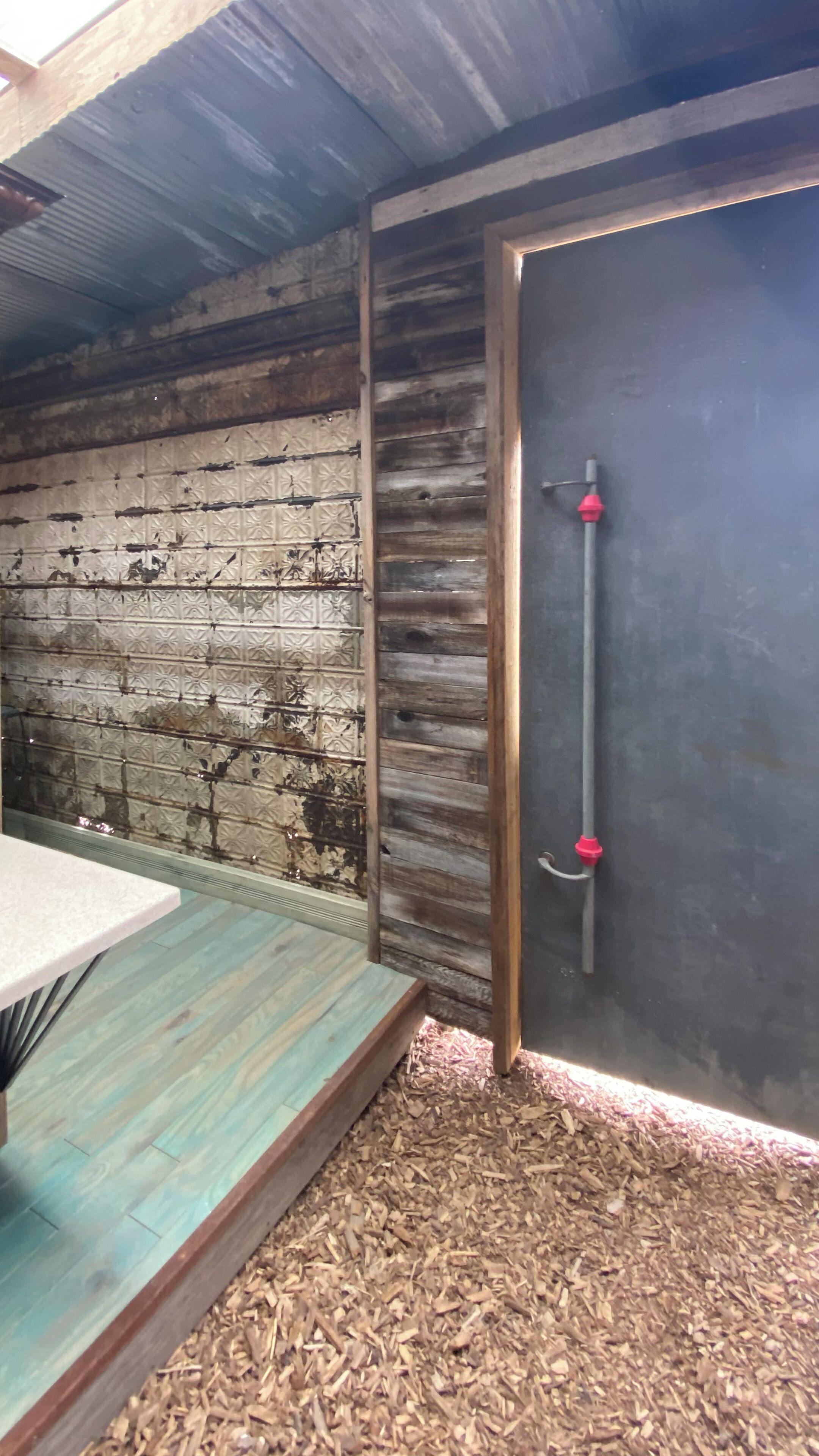 A rustic room with a wooden wall, a metal door with a red handle, and a small table with a white top.