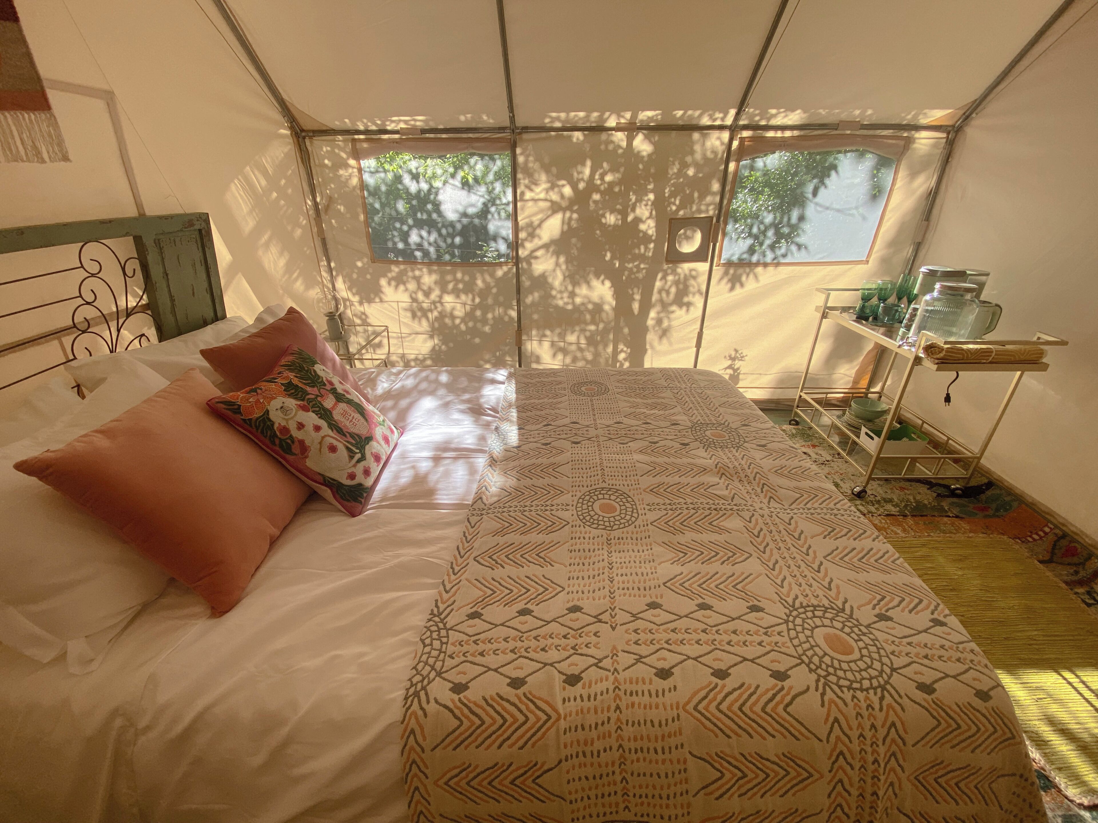 Un dormitorio con cama, almohadas, una ventana y una mesita con objetos.
