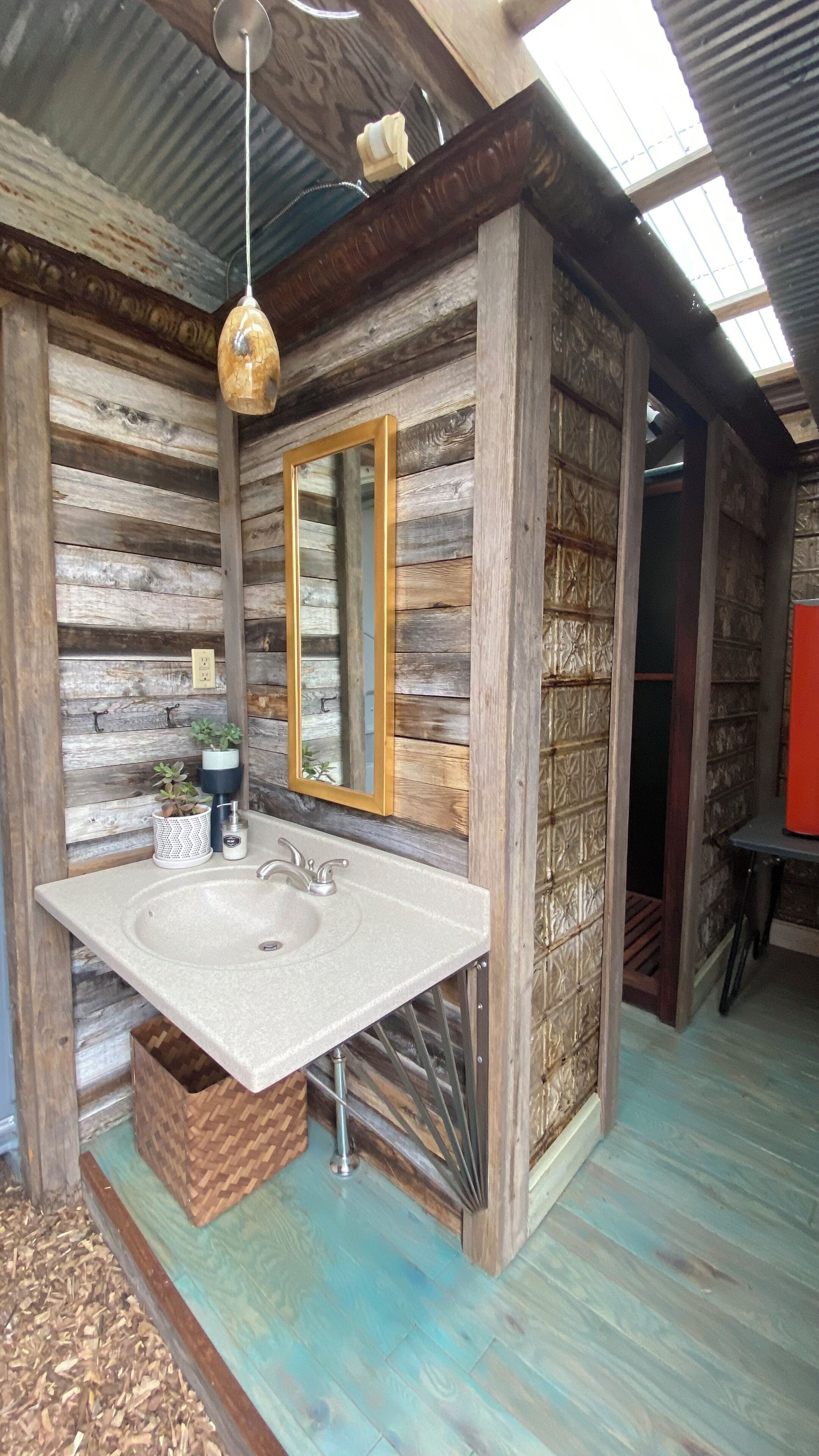 Un baño rústico con pared de madera, un espejo grande, un lavabo y una lámpara colgante.