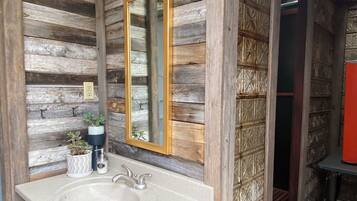 Un baño rústico con pared de madera, un espejo grande, un lavabo y una lámpara colgante.