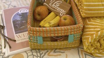 Una cama con una tarjeta de bienvenida, una cesta de mimbre con frutas y una toalla doblada sobre el cubrecolchón.