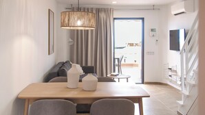 A modern hotel room with a wooden dining table, grey sofas, and a large window with curtains. - Breathtaking sea view, only 100 m to the sea and the beach, heated pool, wifi (Playa de la Américas)