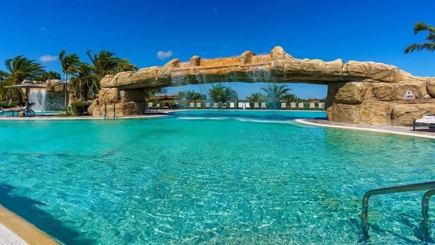 Une piscine d’un bleu éclatant, agrémentée d’une arche naturelle en roche, de chaises longues et de palmiers.