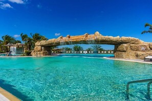 A clear blue pool with a natural rock arch, lounge chairs, and palm trees. - Stunning 2BR/2BA Unit overlooking the scenic Lakewood National Golf Course (Lakewood Ranch)