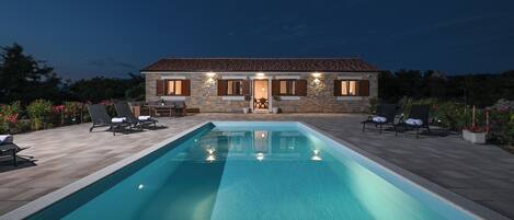 A stone house with a swimming pool, outdoor seating, and a well-lit entrance.