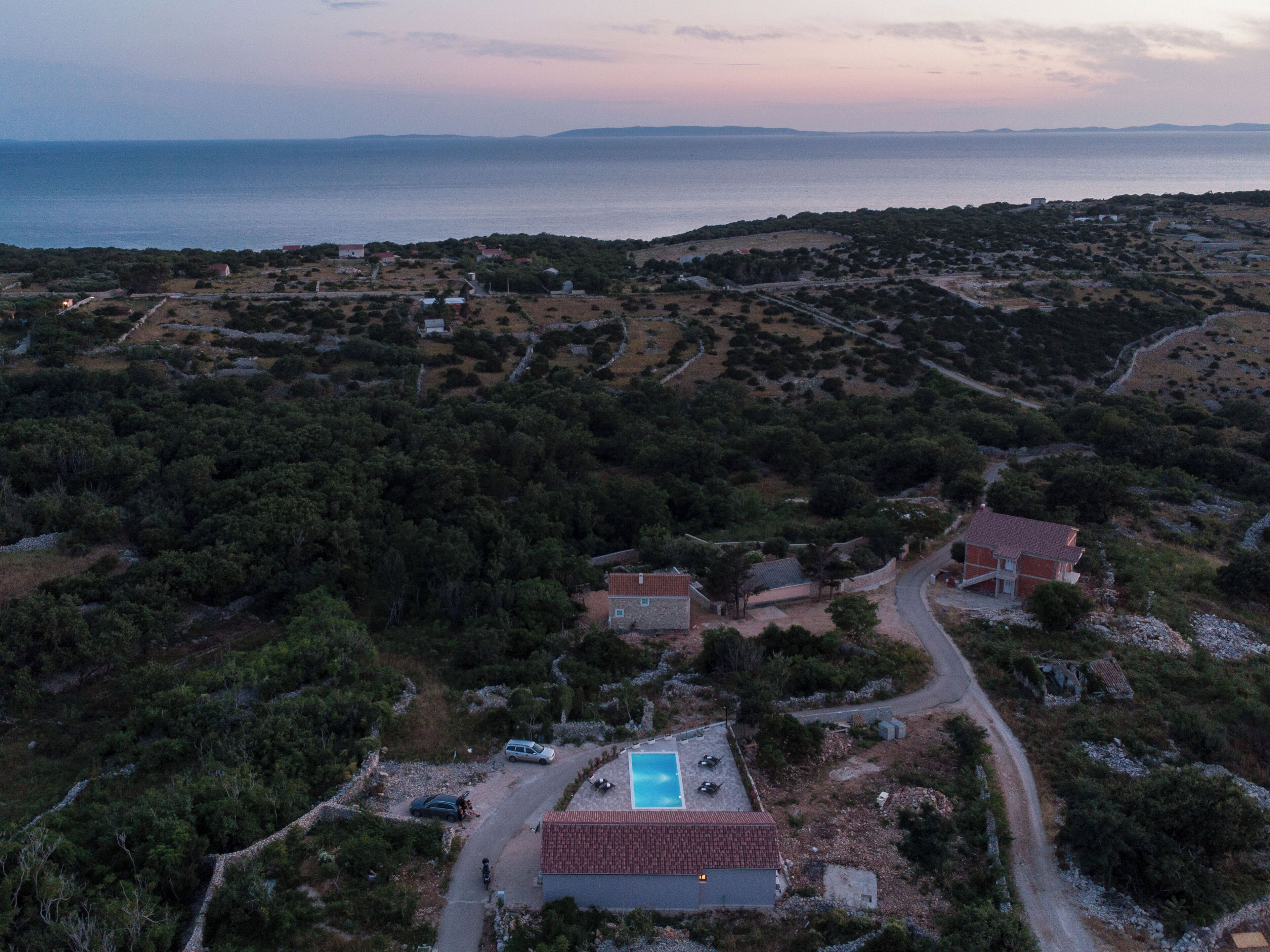 A coastal property with a swimming pool, surrounded by dense vegetation and a view of the sea.