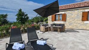 A patio with two black lounge chairs, a table, and a large umbrella. - Villa Nika (Novalja)