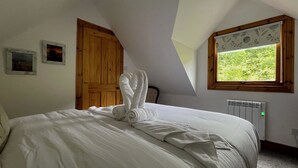 A bedroom with a large bed, a wooden door, a radiator, and a window with a view of greenery.
